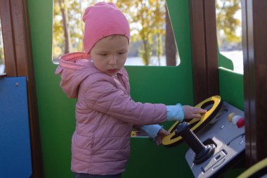 Cute child is playing on the playground with a car simulator. People