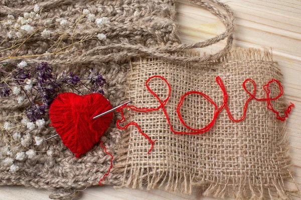 Heart of yarn in cloth and dried flowerson on wooden background. — Stock Photo, Image