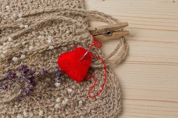 Heart of yarn in cloth and dried flowerson on wooden background — Stock Photo, Image