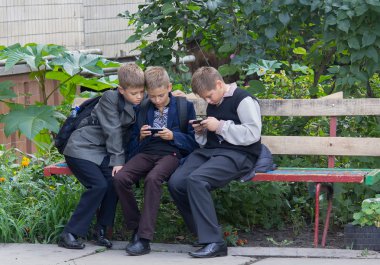 Kiev, Ukrayna - 10 Eylül 2015: Öğrenciler akıllı telefonlar yardımıyla oynanan bankta oturmuş dersten sonra