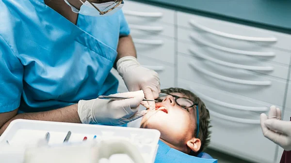 Kovid19 'un genç bir çocuğa temizlik yaptığı için yüz maskesi takan tanınmamış bir diş hekiminin resmi..