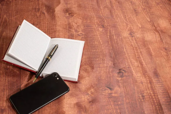Masanın üzerinde akıllı telefon ve kalem olan defter.