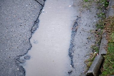 Kırık asfalt, su birikintisi ve yağmur damlası. Yukarıdan görüntüle.