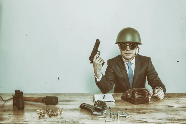 Vintage military businessman sitting at office desk with hand gun