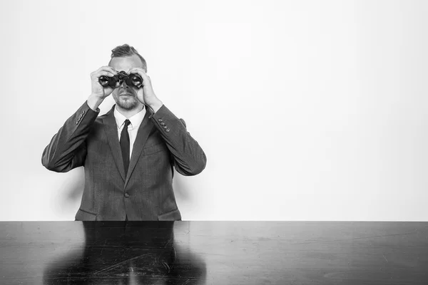 Empresário sentado na mesa do escritório com binóculos — Fotografia de Stock