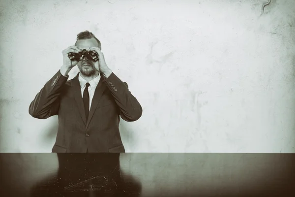 Businessman sitting at office desk with binoculars — Stock Photo, Image