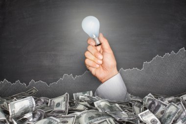 Ampul tutan el ile yazı tahtası üzerinde para yığını