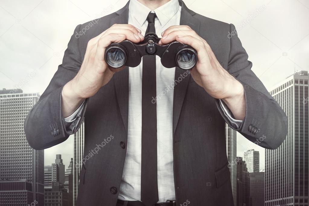 Businessman holding binoculars on cityscape background