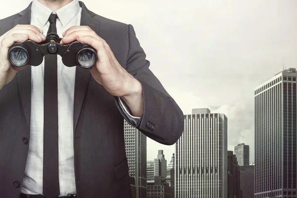 Empresário segurando binóculos no fundo da paisagem urbana — Fotografia de Stock