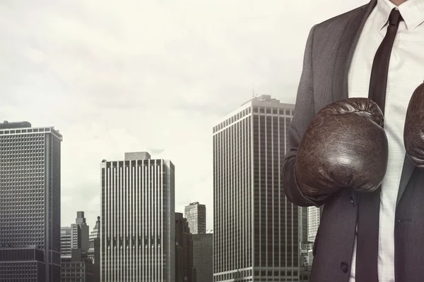 Businessman in boxing gloves on cityscape background — Stock Photo, Image