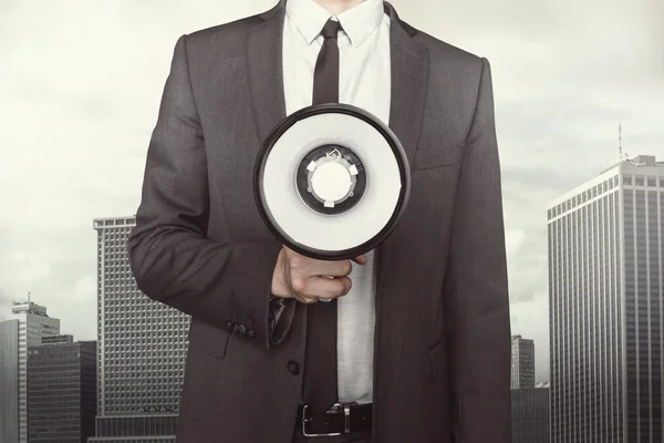Бизнесмен держит мегафон на фоне городского пейзажа — стоковое фото