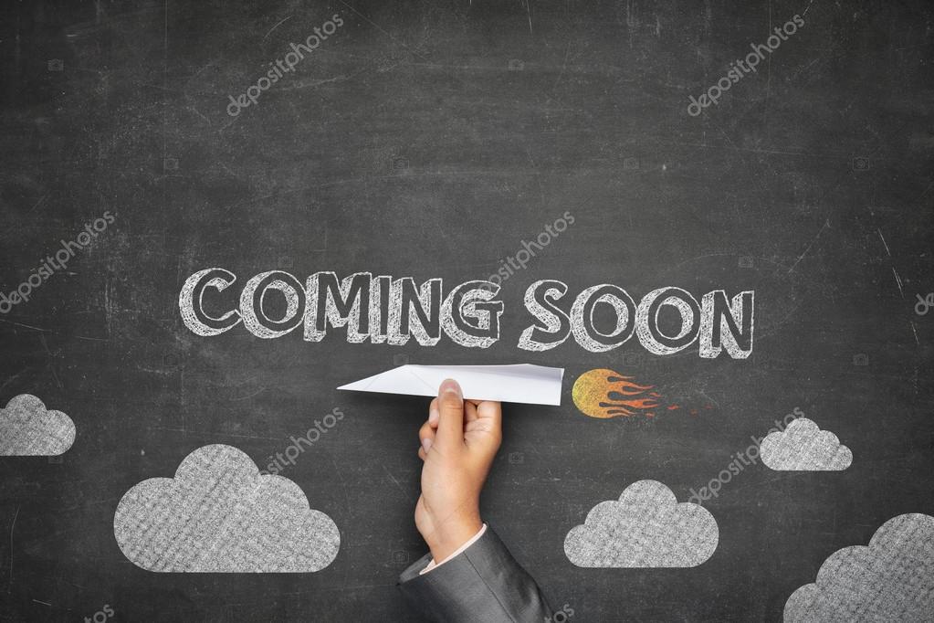 Coming soon concept on black blackboard with businessman hand holding paper plane
