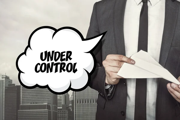 Under control text on speech bubble with businessman holding paper plane in hand — Stock Photo, Image