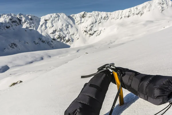 Down mittens clipped carabiner on a yellow ice axe and a ridge in the background. — Stock Photo, Image