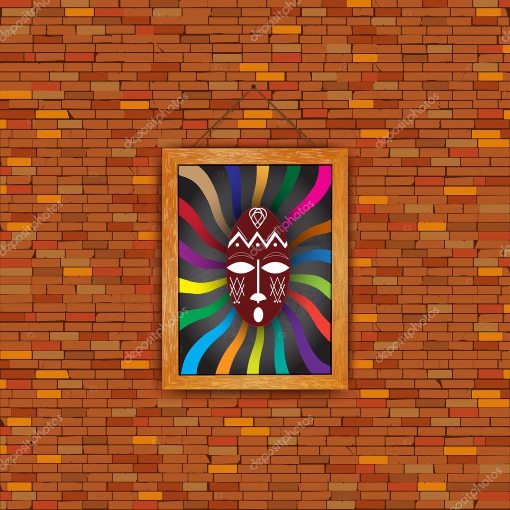 On a brick wall in a wooden picture frame hanging old. The painting depicts a shaman's mask from Africa, America, Australia, in the traditional style. The mask on the background of multi-colored beams with a black background.