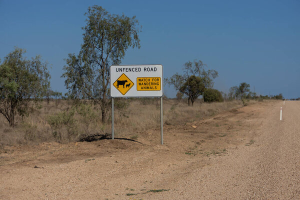 Sign beside an unfenced, unsealed dirt road in outback Queensland, Australia advising road is not fenced and to watch for cattle.