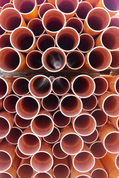 A stack of orange electrical PVC conduit pipes in rows end on giving a repeat pattern of circles.