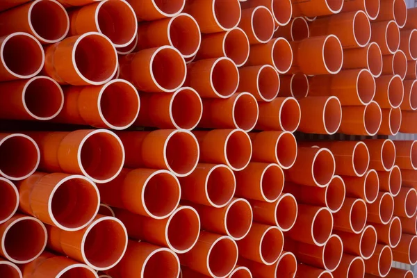 A stack of orange electrical PVC conduit pipes in rows end on giving repeat patterns of circles.