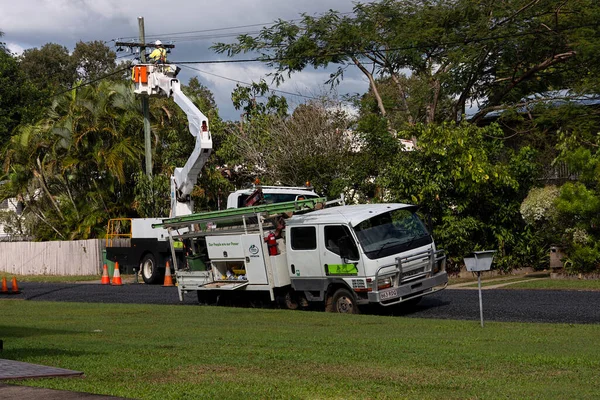 Walkerston, Queensland, Avustralya - 9 Temmuz 21 Temmuz, elektrik işçisi bir kova kamyonunda elektrik direği üzerinde çalışıyor ve arkasında bulutlu bir gökyüzü ve tropikal bitki örtüsü ile yeni kablolar asıyor..
