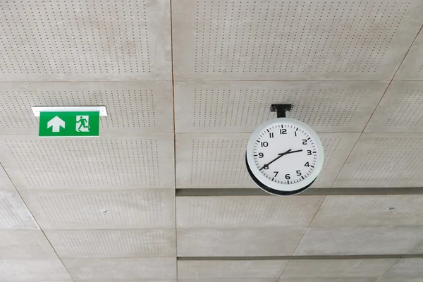 Relógio círculo moderno e sinal de saída pendurar no teto sob edifício de escritórios — Fotografia de Stock