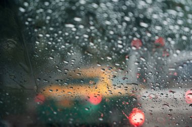 Yağmur damlaları arabanın ön camına içeriden bakıyor. Şiddetli yağmur fırtınası sırasında trafik sıkışıklığı