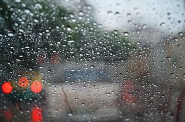 Yağmur damlaları arabanın ön camına içeriden bakıyor. Şiddetli yağmur fırtınası sırasında trafik sıkışıklığı