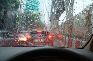 Yağmur damlaları arabanın ön camına içeriden bakıyor. Şiddetli yağmur fırtınası sırasında trafik sıkışıklığı