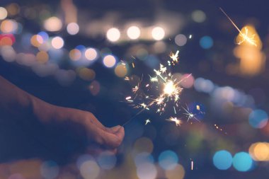 Bokeh arka planında maytap tutan kadın eller. Kutlama için yanan maytap, festival partisi geçmişi.