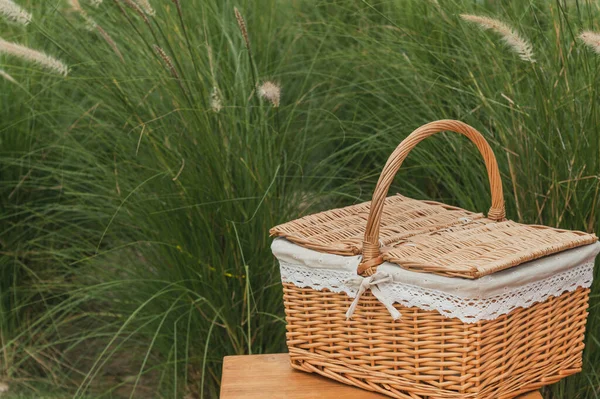 Woven wood picnic basket on small wooden table in park. Summer sunny day and picnic time concept