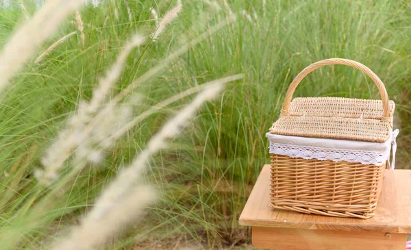 Woven wood picnic basket on small wooden table in park. Summer sunny day and picnic time concept