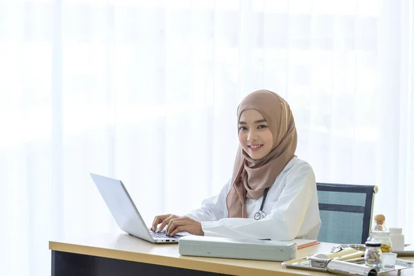Jeune Femme Asiatique Musulmane Médecin Sourire Regarder Caméra Tout Travaillant Photo De Stock