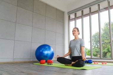 Yoga yapma zamanı. Ardha Padmasana egzersizinde oturan genç çekici bir kadın, Lotus meditasyonda poz veriyor, gözleri kapalı, evde spor kıyafetleri giyiyor. yaşam tarzı konsepti