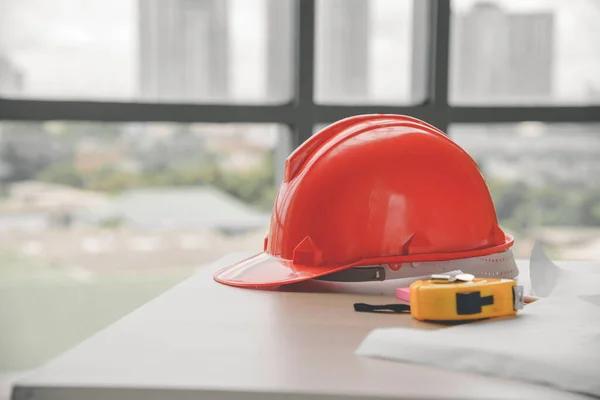 Red hard safety helmet hat, yellow tape measure (measuring tape) and blueprint on table in office worker conference site with copy space. Engineering tools concept