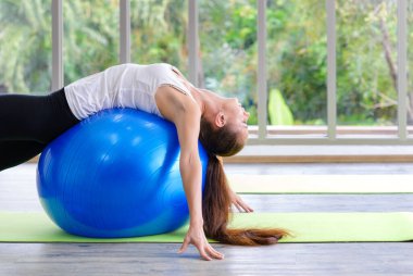 Beyazlı kadın egzersiz topuyla egzersiz yapıyor. Fitness kızları spor salonunda karın kaslarını uygun topla esnetiyorlar.