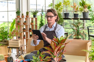 Mutlu bahçıvanlık, gözlük takan, kot önlüklü, dijital tabletli, bahçe işleriyle uğraşan ve ağacı kimin aldığına bakan biri. Küçük işletme kavramı.