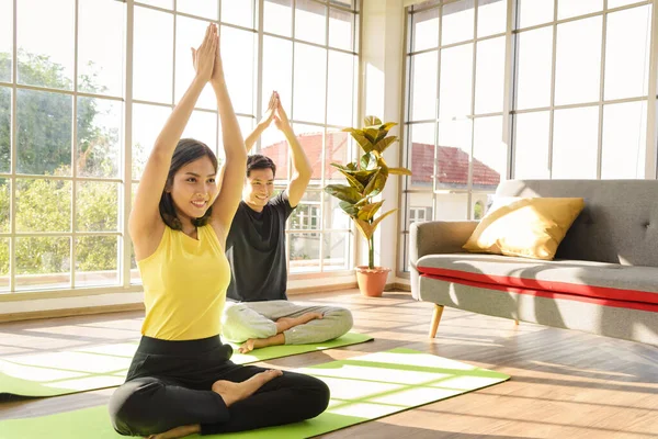 Young Asia couple practicing yoga lesson, breathing and meditating together in living room at home. healthy lifestyle concept