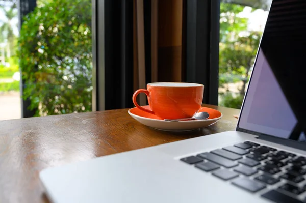 Kafe Içindeki Ahşap Masada Modern Dizüstü Bilgisayarlı Bir Fincan Sıcak — Stok fotoğraf