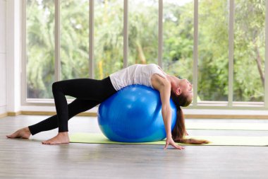 Beyazlı kadın egzersiz topuyla egzersiz yapıyor. Fitness kızları spor salonunda karın kaslarını uygun topla esnetiyorlar.