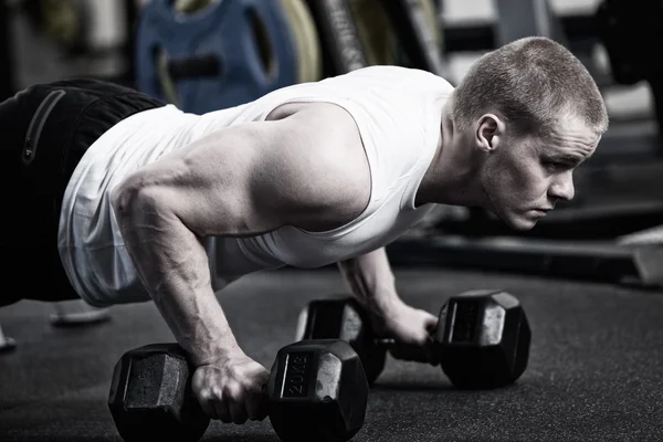 Foto Man gör push upp hålla hantel på gymmet — Stockfoto