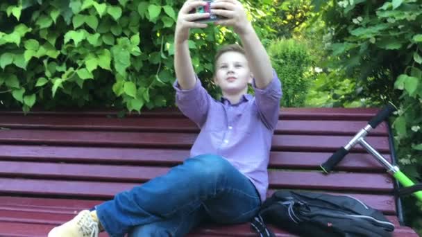 En pojke sitter på bänken och gör selfie — Stockvideo