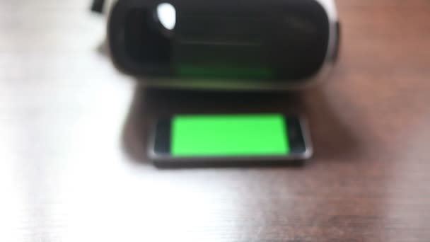 3D ακουστικά και ένα κινητό τηλέφωνο στο τραπέζι. Πράσινο φόντο — Αρχείο Βίντεο