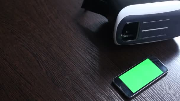 Auriculares 3D y un teléfono móvil sobre la mesa. Fondo verde — Vídeo de stock