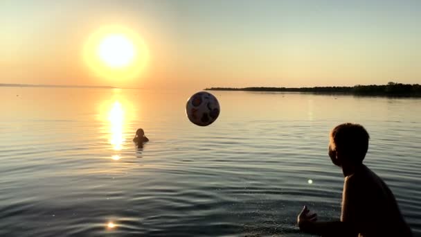 Niños jugando pelota en el agua al atardecer . — Vídeo de stock