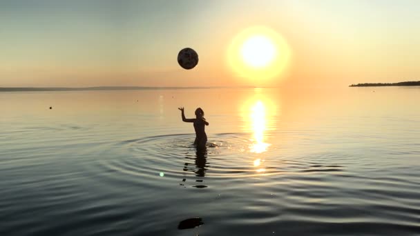 Niños jugando pelota en el agua al atardecer . — Vídeo de stock