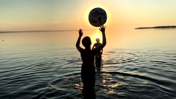 Діти грають у м'яч у воді на заході сонця . — стокове відео