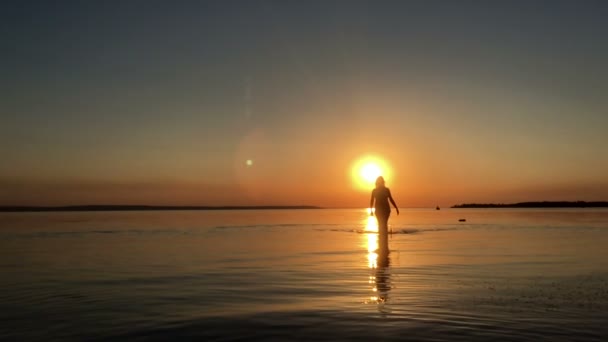 Menina caminha na água ao pôr do sol — Vídeo de Stock