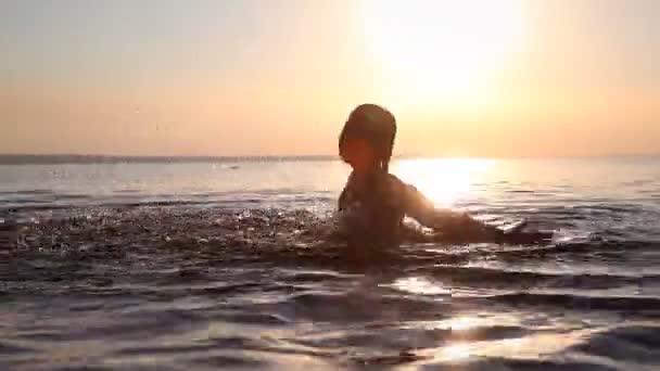 Una joven salpica agua al atardecer — Vídeos de Stock