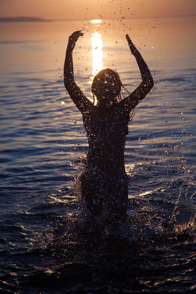 Jeune fille éclabousse l'eau au coucher du soleil Images De Stock Libres De Droits