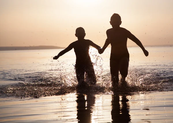 Les enfants courent le long de l'eau au coucher du soleil Photo De Stock