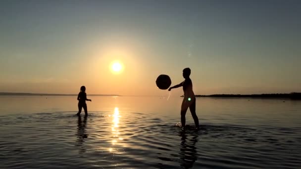 Barn spelar bollen i vattnet vid solnedgången. — Stockvideo